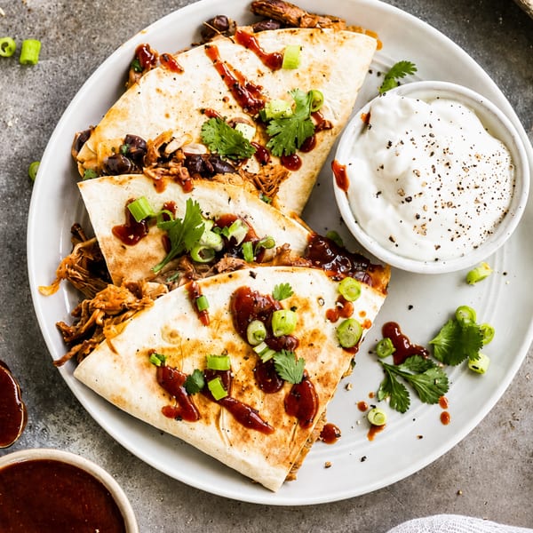Pulled pork quesadillas with black beans, BBQ sauce, cilantro, and green onions, served with sour cream.
