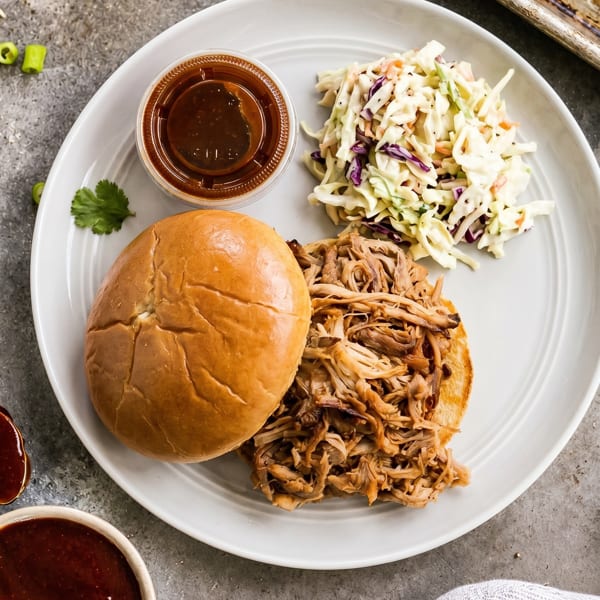 Pulled pork sandwich with coleslaw and barbecue sauce on a white plate, overhead view.