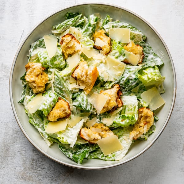 Caesar salad with romaine lettuce, creamy dressing, croutons, and parmesan cheese in a bowl.